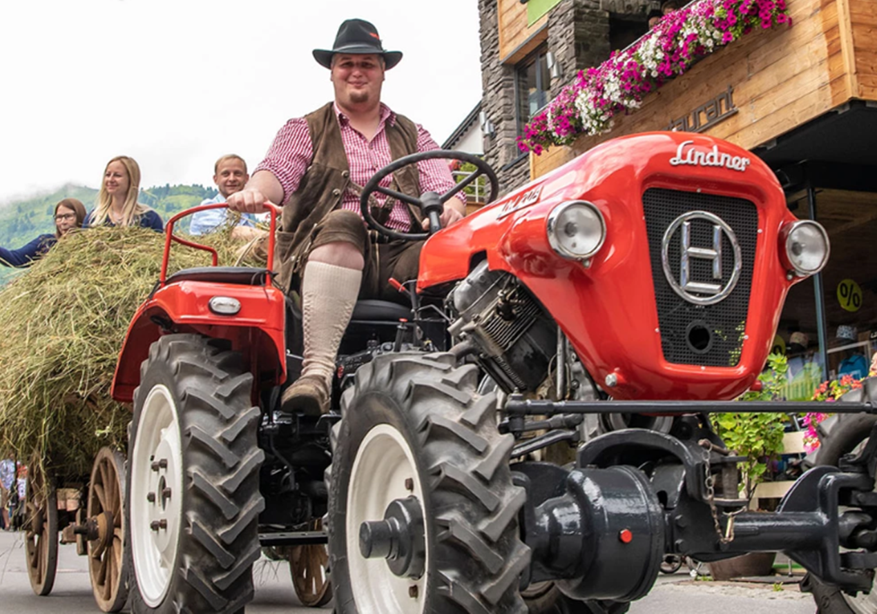 Traktor mit Heuwagen und Menschen beim Dorffest am Arlberg.