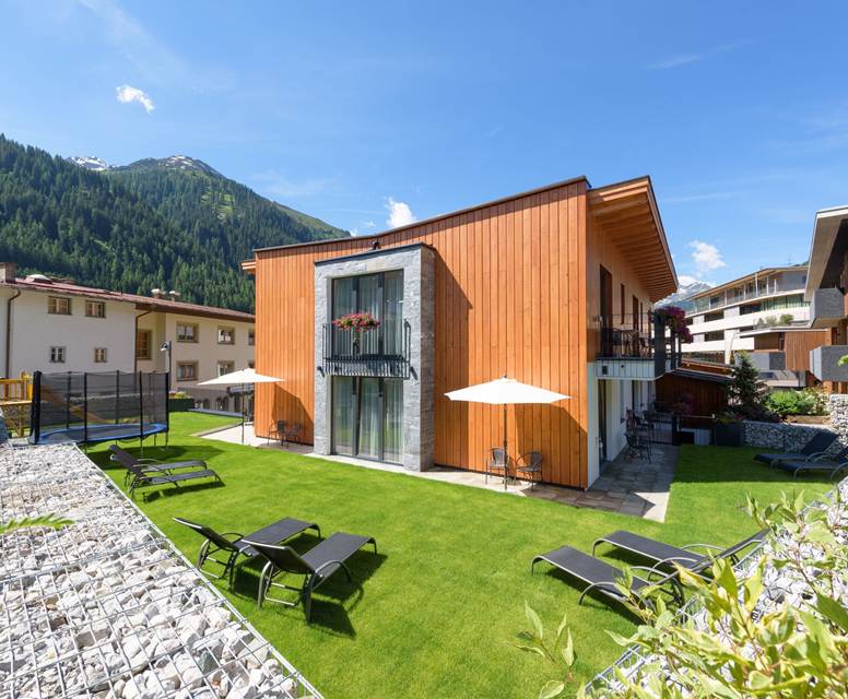 Sonniger Gartenbereich mit Liegestühlen und Terrasse bei den Apartments am Arlberg.
